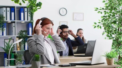 working day, young female and male colleagues put on headsets to communicate with clients and talk on video call while sitting at laptops in office - Powered by Adobe