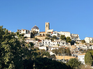 Obraz premium Scenic view of Altea village with whitewashed houses, a blue-tiled dome, and a bell tower on a hillside under a clear blue sky