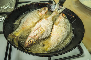 three whole freshwater fish frying with flour in old cast iron skillet
