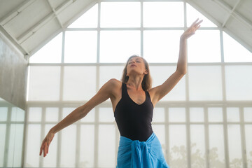 Fototapeta premium A close-up portrait of a woman dancer gracefully moving her arms and head during a contemporary dance performance in a bright studio. Her expression reflects passion and elegance.