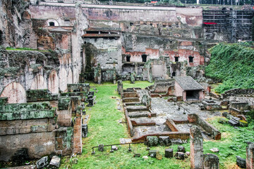 A large building in Rome Italy with a lot of bricks and a grassy area in front of it. There are many people walking around the area