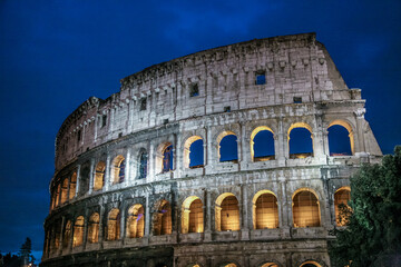 The Colosseum in Rome Italy is lit up at night. The building is very large and has many windows