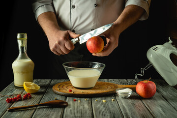 Hands skillfully slice an apple beside a mixing bowl filled with creamy ingredients, surrounded by fresh fruit and a bottle of liquid. The warm glow enhances the inviting atmosphere of cooking