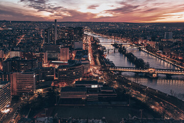 A Paris city at night with a river running through it. The city is lit up with lights. There are...