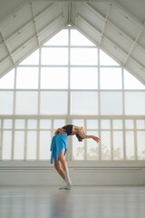 Fototapeta premium A ballerina rehearses in a bright, minimalist studio with large windows. Her elegant pose highlights ballet, grace, and poise, capturing the art and dedication of professional dance practice.