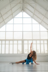 A medium shot of a woman gracefully stretching and preparing her body for a contemporary dance session in a bright, spacious studio. Her pose exudes focus and poise