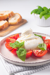 Delicious Italian caprese salad with sliced mozzarella, tomatoes, basil, and bread on background. 