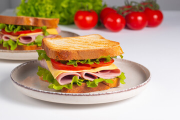 Close-up of two sandwiches with bacon, salami, prosciutto and fresh vegetables on rustic wooden cutting board. Club sandwich concept