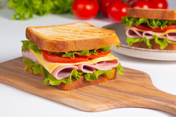 Close-up of two sandwiches with bacon, salami, prosciutto and fresh vegetables on rustic wooden cutting board. Club sandwich concept