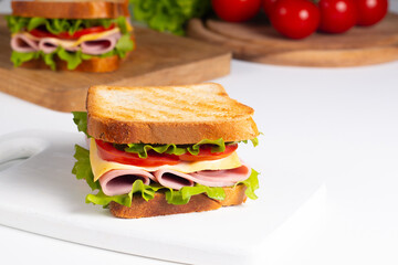 Close-up of two sandwiches with bacon, salami, prosciutto and fresh vegetables on rustic wooden cutting board. Club sandwich concept