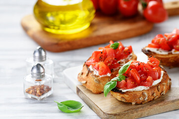 Cherry tomatoes and cream cheese bruschettas with fresh basil leaves on white wooden background 