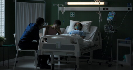 Young mother sits next to her child who is lying unconscious in an oxygen mask.