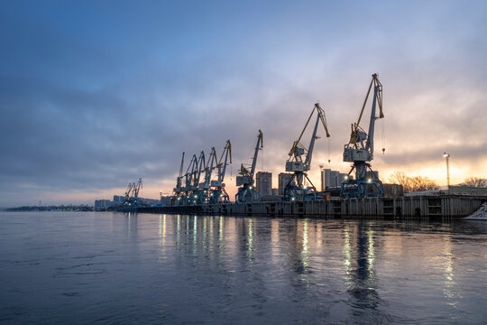 A beautiful industrial seaport or river port at dawn with cranes and calm waters. Cargo transportation shipping and logistics