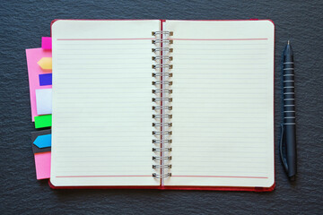 Open spiral bound notebook with blank pages and colorful bookmarks. Dark background, flat lay, copy space