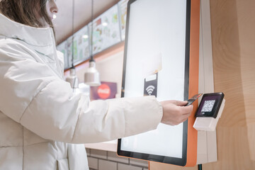 A satisfied customer is using a contactless payment system at a modern fast food kiosk, enjoying...