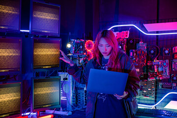 Asian woman in front of a computer monitor display big digital data with laptop computer, neon light, Hacker wear black jacket at system control room, Security guard working on multiple monitors