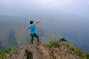 Obraz premium Misty scenery of viewpoint Rock Ella in Sri Lanka with silhouette of standing woman with raised arms in blue shirt.