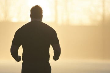 A man is running in the woods with the sun setting in the background