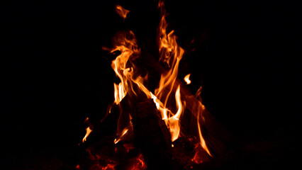 firewood burns, fire coals at night. Red hot coals glowing on a dying campfire pit. Orange glow from the coals at the stake at night. flames on a black background