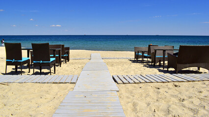 tables and a wooden walkway to the sea. A wooden walkway leading from the beach to the sea with a bright blue sky. hot summer, blue warm sea. rest, vacation
