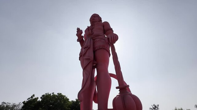Giant red Hanuman statue in Delhi, India, viewed from bottom to top under clear sunlight. Iconic Hindu deity with a mace, traditional attire, sacred monument, and cultural landmark.