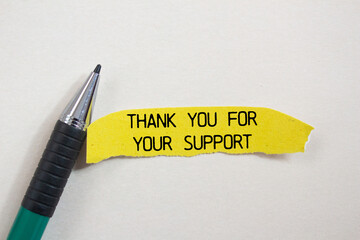Thank you for your support message written on ripped torn yellow paper piece and a pen with white...