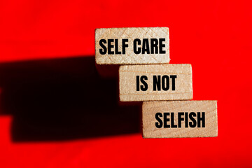 Self care is not selfish message written on wooden blocks on red background. Conceptual self care is not selfish symbol. Copy space.