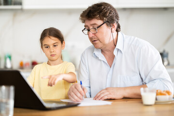 Fototapeta premium Father helps daughter do homework using laptop