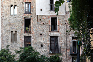 Old stone wall of a residential building with balconies and windows in the city, amidst greenery. From the series windows of the world.