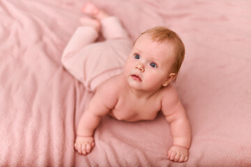 Young red-haired female child on soft pink blanket gazes upward. Light complexion, curious expression. Warm lighting, textured background adds coziness