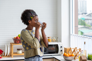 Young African black woman sipping coffee in cozy modern kitchen with natural light and fruits