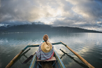 Fototapeta premium Rear View of Woman on Traditional Boat at Sunrise Over Lake Batur in Bali, Indonesia.