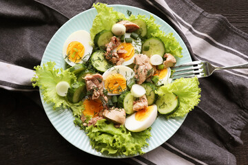 Salad from the liver of codfish, eggs, lettuce and cucumber on a  plate on a dark wooden background. Top view. Copy space.