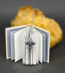 A cross on the white paper. There is a yellow stone in defocus in the background. Prayer. Easter. The Bible