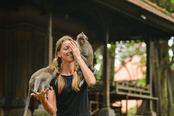 Smiling tourist woman interacting with monkeys at a sacred monkey forest temple in Bali.