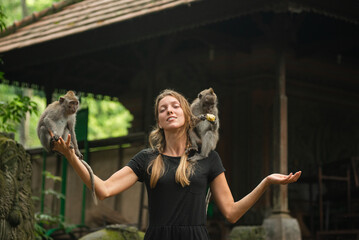 Smiling tourist woman interacting with monkeys at a sacred monkey forest temple in Bali. © Evgenii
