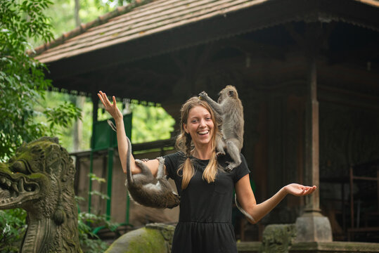 Smiling tourist woman with monkeys in Bali monkey forest temple.