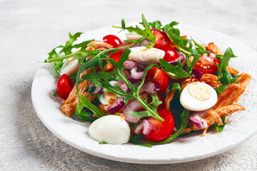 a warm salad with fried chicken fillet, arugula and cherry tomatoes, and boiled quail eggs, on a white plate, no people.