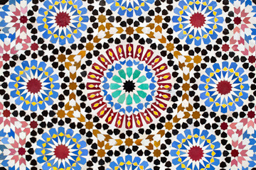 A detailed Islamic geometric mosaic featuring vibrant colors and symmetrical patterns. The design showcases traditional arabesque motifs with star shapes and interwoven lines