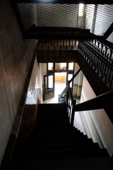 View of wooden stairs going down in the dark with light from the bottom floor.