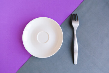 Empty plate and fork on grey and purple background. Copy space for the text. Minimal concept