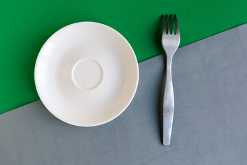 Empty plate and fork on grey and green background. Copy space for the text. Minimal concept