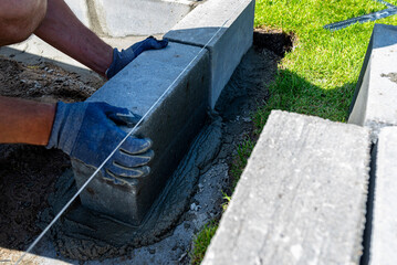A man lays concrete blocks on a poured foundation, gluing them with mortar.