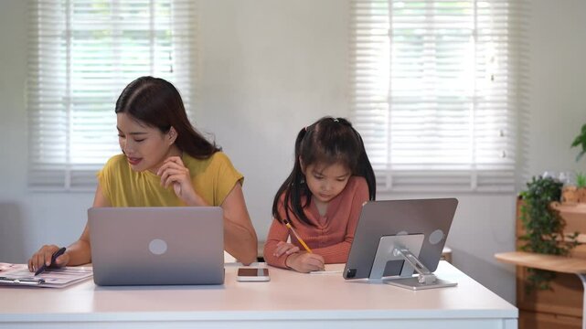 A mother juggles a phone call while helping her daughter with homework, demonstrating multitasking and care in a home setting.
