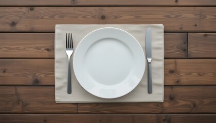 A high-angle, close-up view of a wooden table setting. A white plate, a fork, and a knife are arranged on a beige linen napkin. The plate is centered in the image, with the fork and knife positioned 