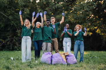 Group of volunteers cheering after cleaning park trash in garbage bags
