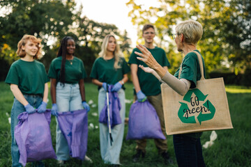 Group of volunteers picking up trash in park are discussing about environmental issues