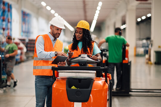 Warehouse workers using digital tablet and driving forklift in logistics center