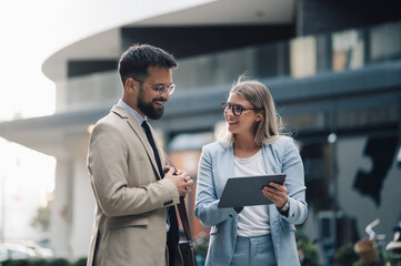 Business people having conversation about work outdoors while using digital tablet