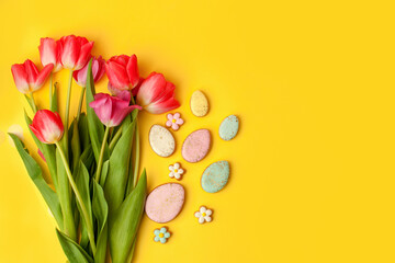 Happy Easter. Multi-colored pastel easter cookies gingerbread, seasonal flowers tulips on yellow background. Easter concept, copy space, flyer, banner, coupon, greeting card, invitation